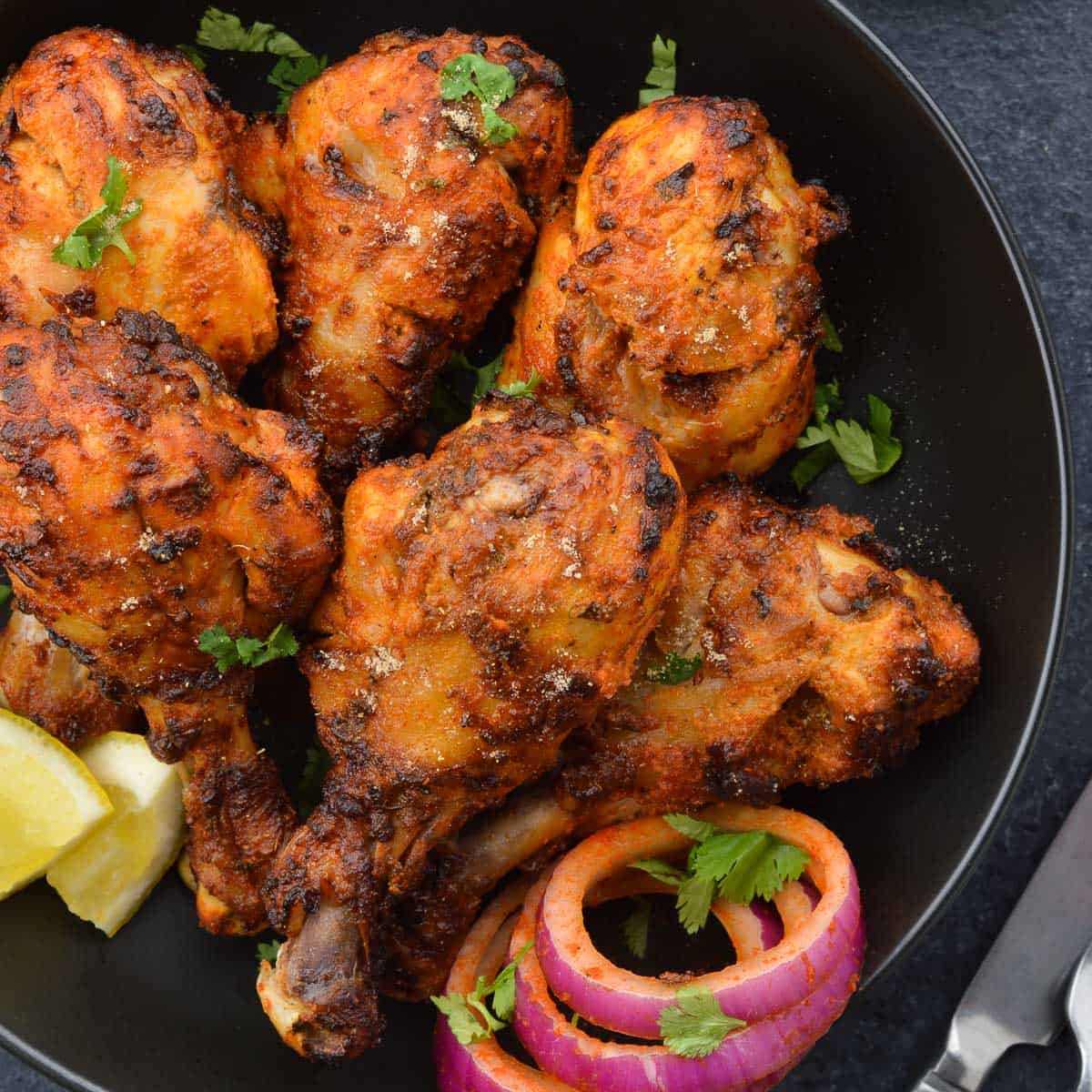 air fried tandoori chicken drumsticks in a bowl, along with laccha pyaaz, a couple lemon wedges & chopped coriander leaves.