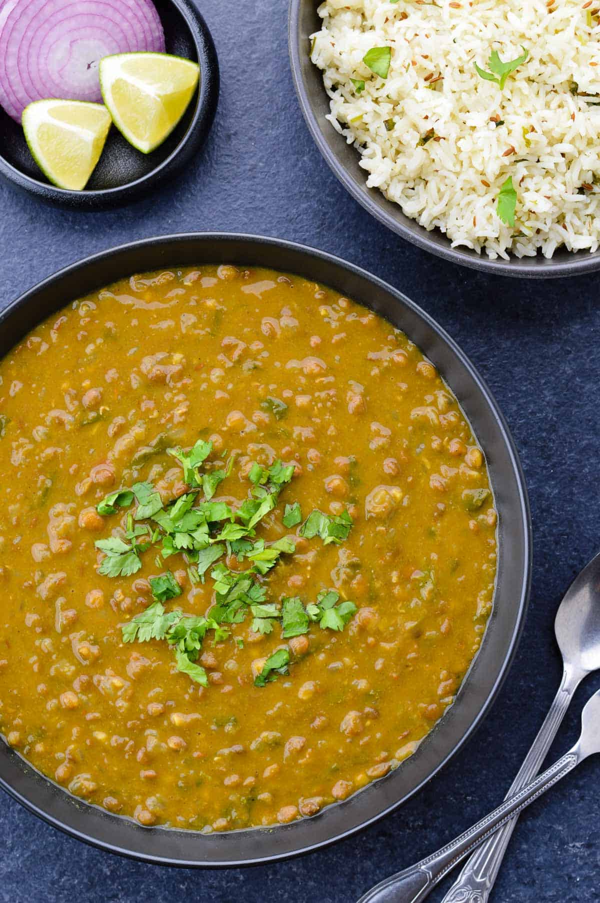 close up shot of whole masoor dal tadka in a big bowl, with a bowl of jeera rice on the side.