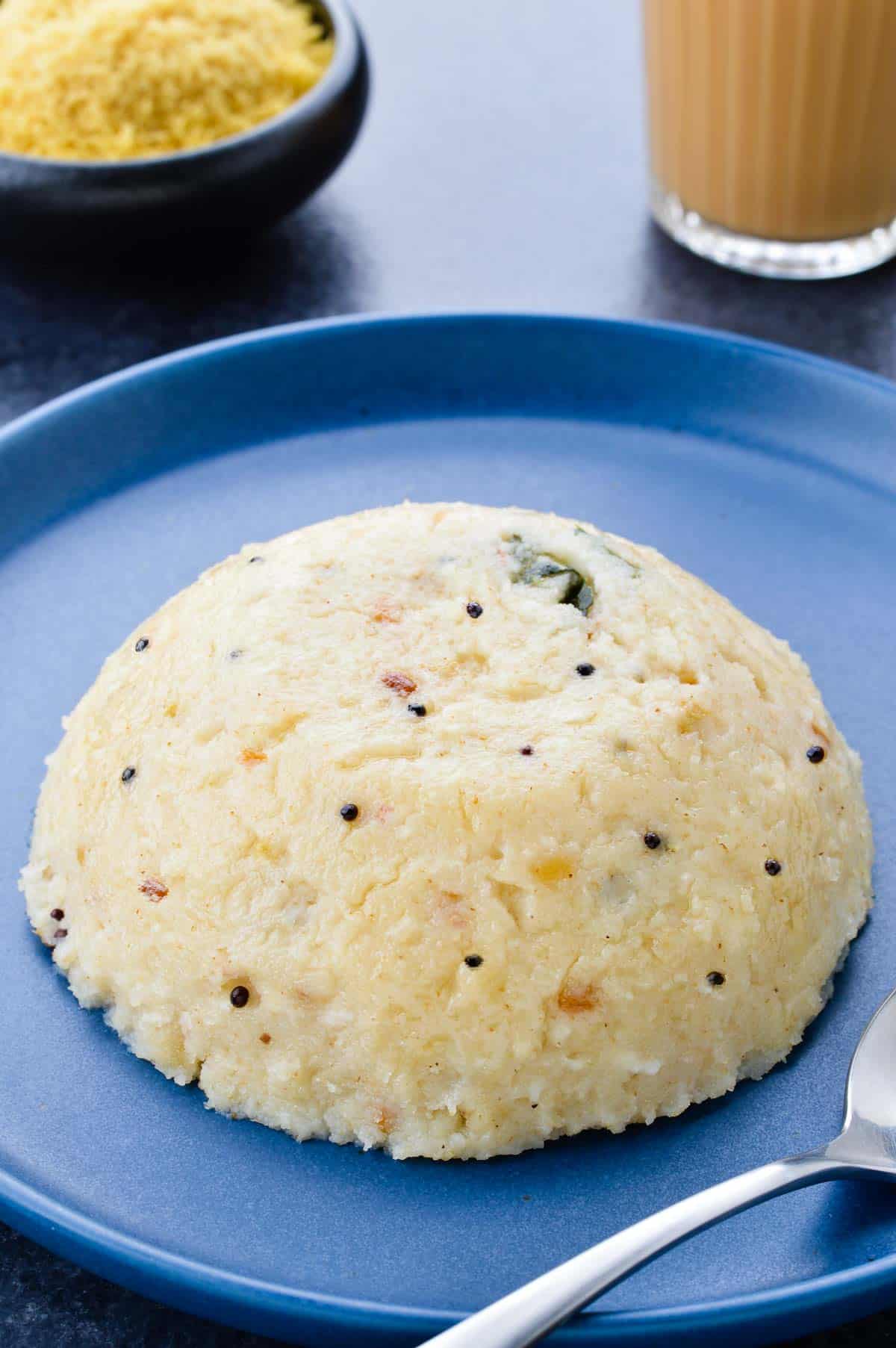 soft rava upma served in a plate, along with a glass of tea, and a small bowl of sev on the side.