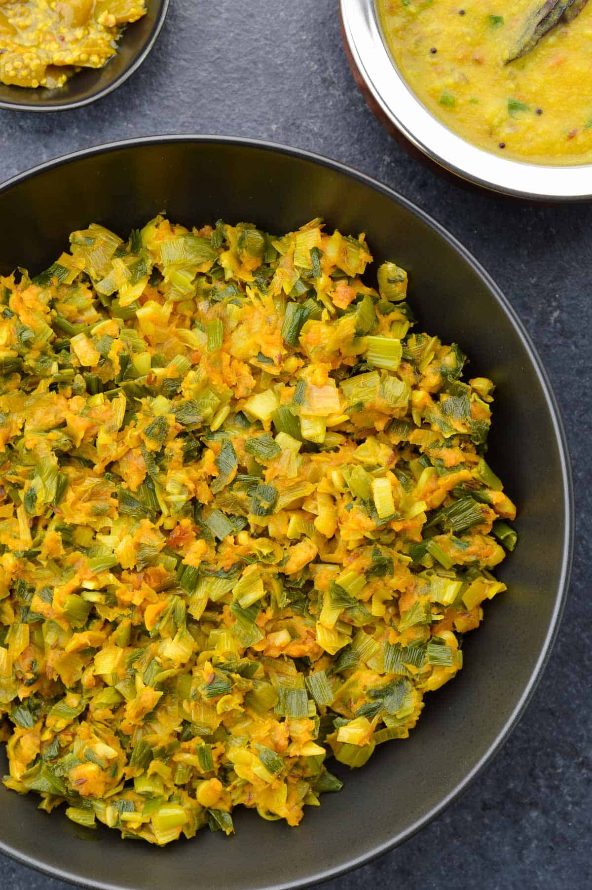 a big serving bowl of spring onion sabzi, along with a pot of dal on the side, and a small bowl of pickle.